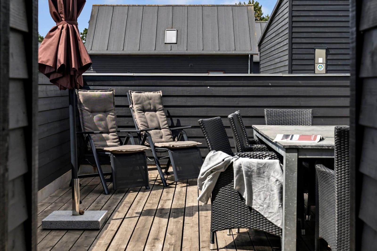 Zwei Liegestühle mit Kissen stehen auf einer Holterrasse vor einer schwarzen Wand.