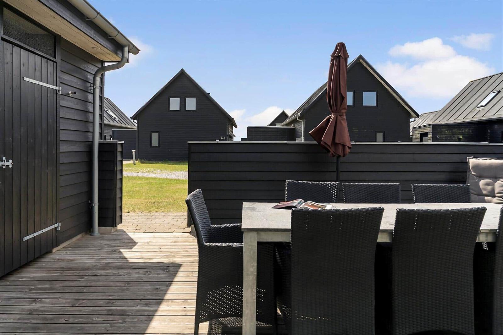 Terrasse mit Tisch und Stühlen, Grill und Glasfront zum Haus.
