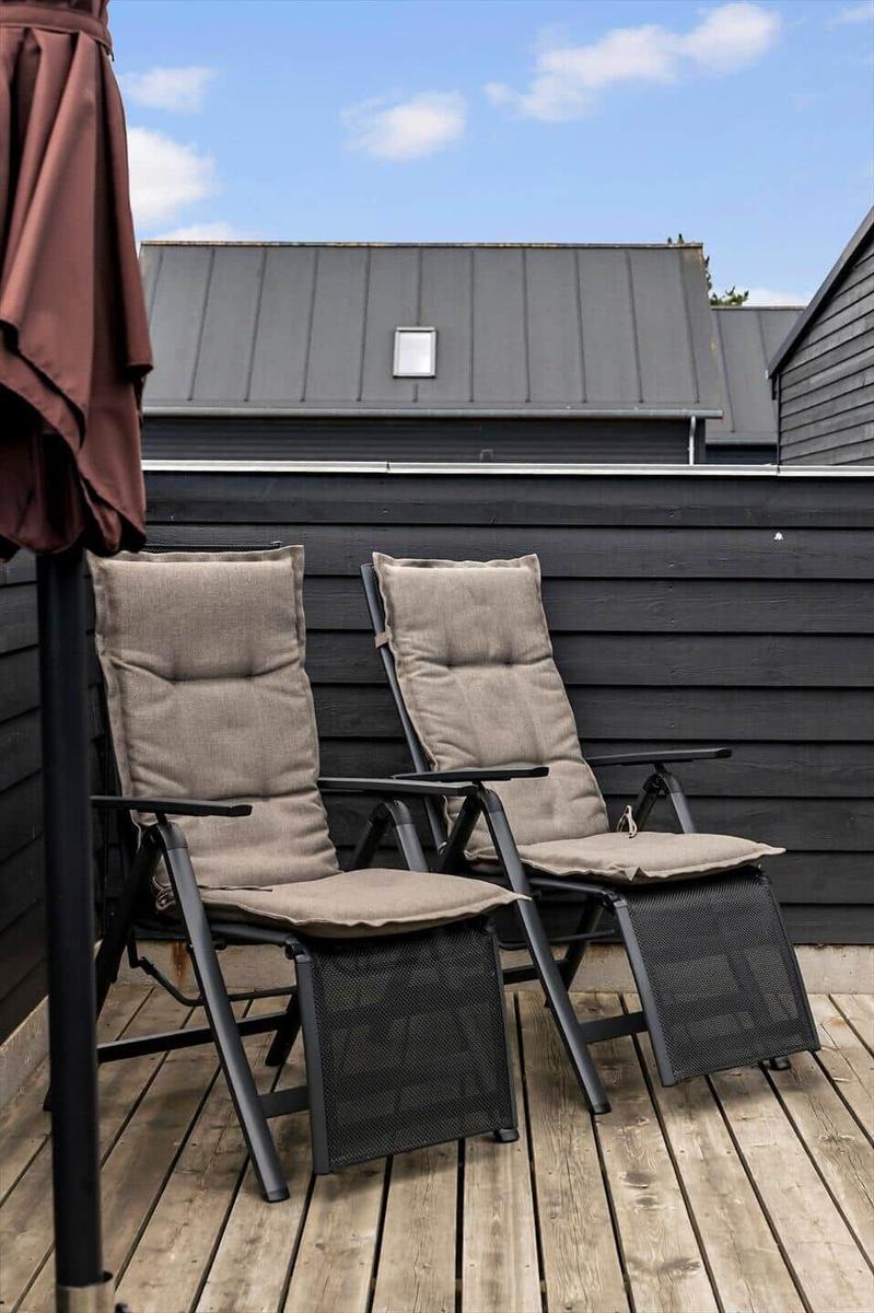 Terrasse mit Liegestuhl, Tisch und Stühlen. Glasfront öffnet zum Innenraum.