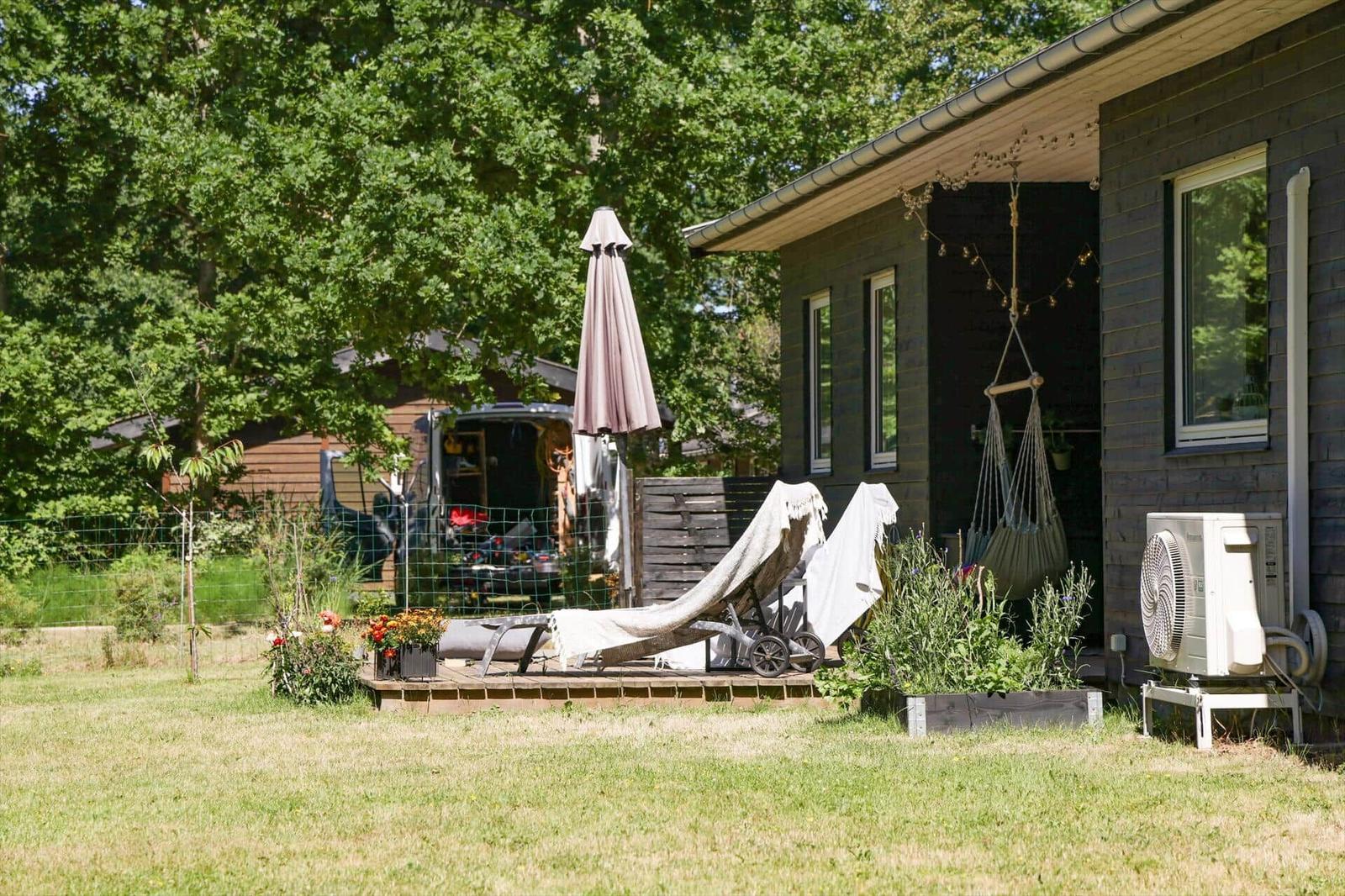 Ein Trampolin mit Sicherheitsnetz steht auf einer grünen Wiese umgeben von Bäumen.