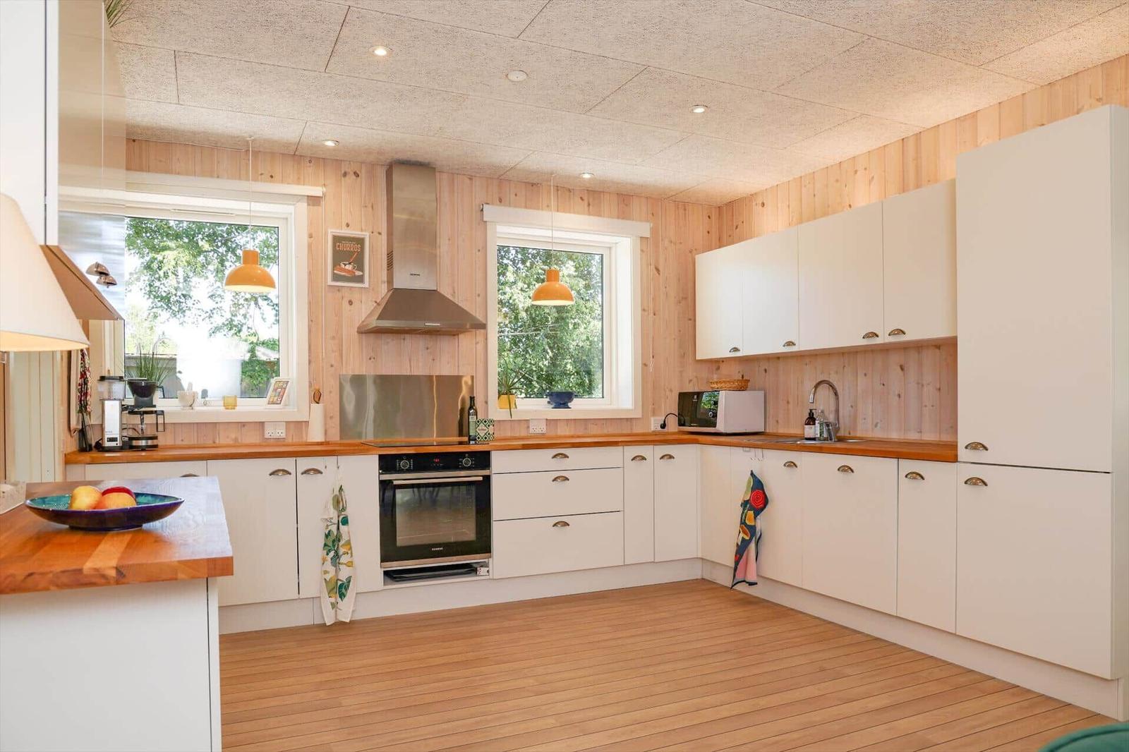 Wohnzimmer mit L-förmigem Sofa, Holzwand und Fenstern. Es gibt einen Tisch und eine Decke.