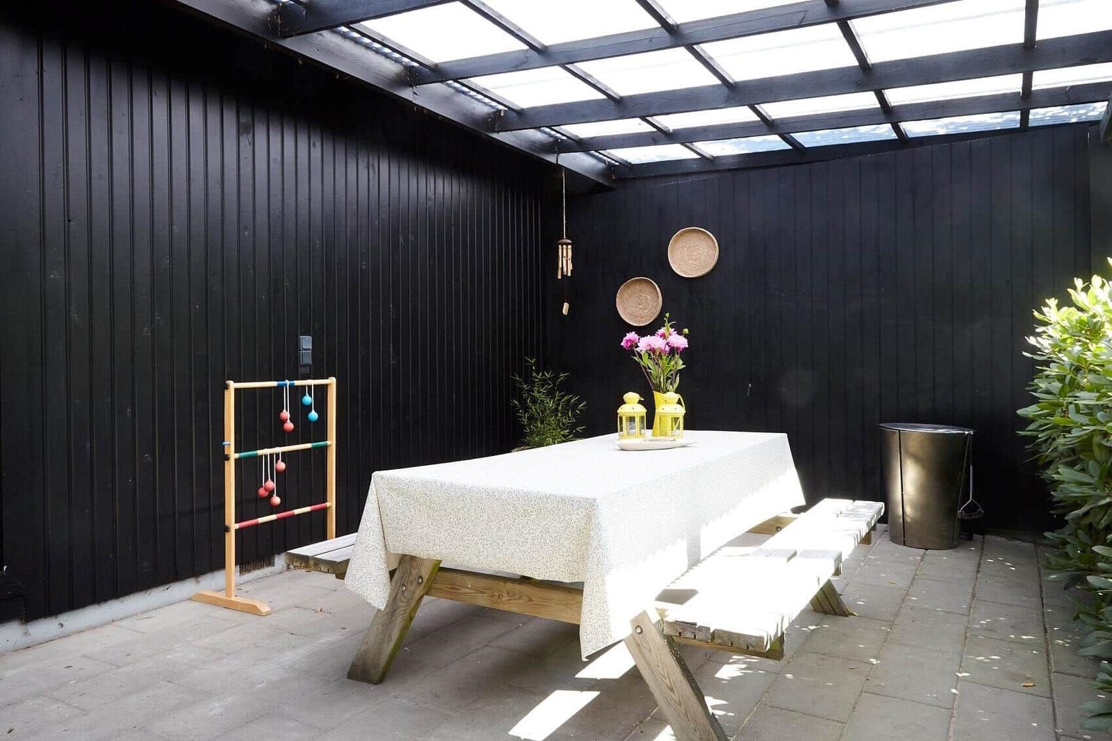 Gedeckter Balkon mit Tisch, Bänken und Blumen. Grün umgebende Landschaft.