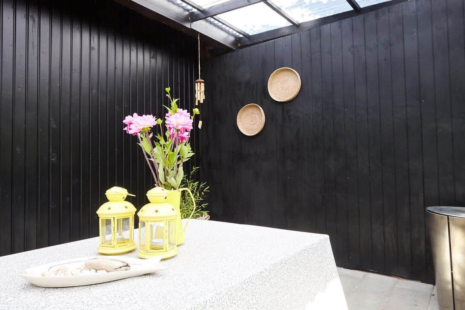 Ein schwarzes Haus mit Glasfront und Garten. Hinter dem Haus sind Bäume zu sehen.