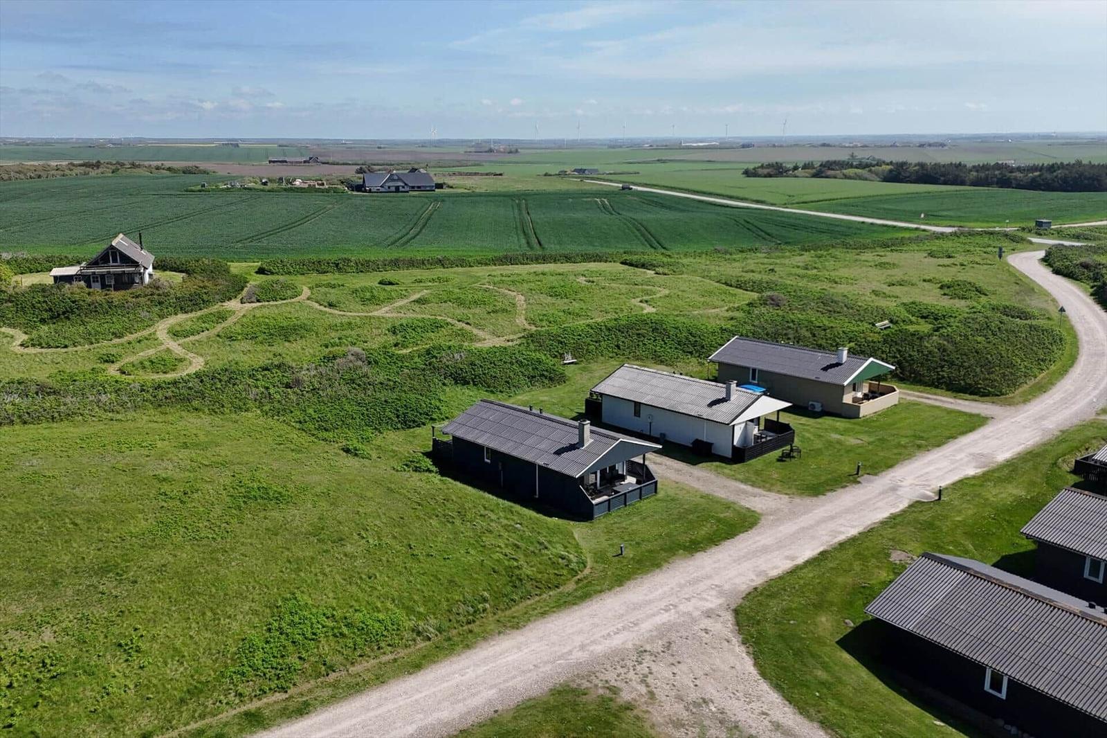 Aerial view of vacation homes on green landscape with dirt roads and distant fields.