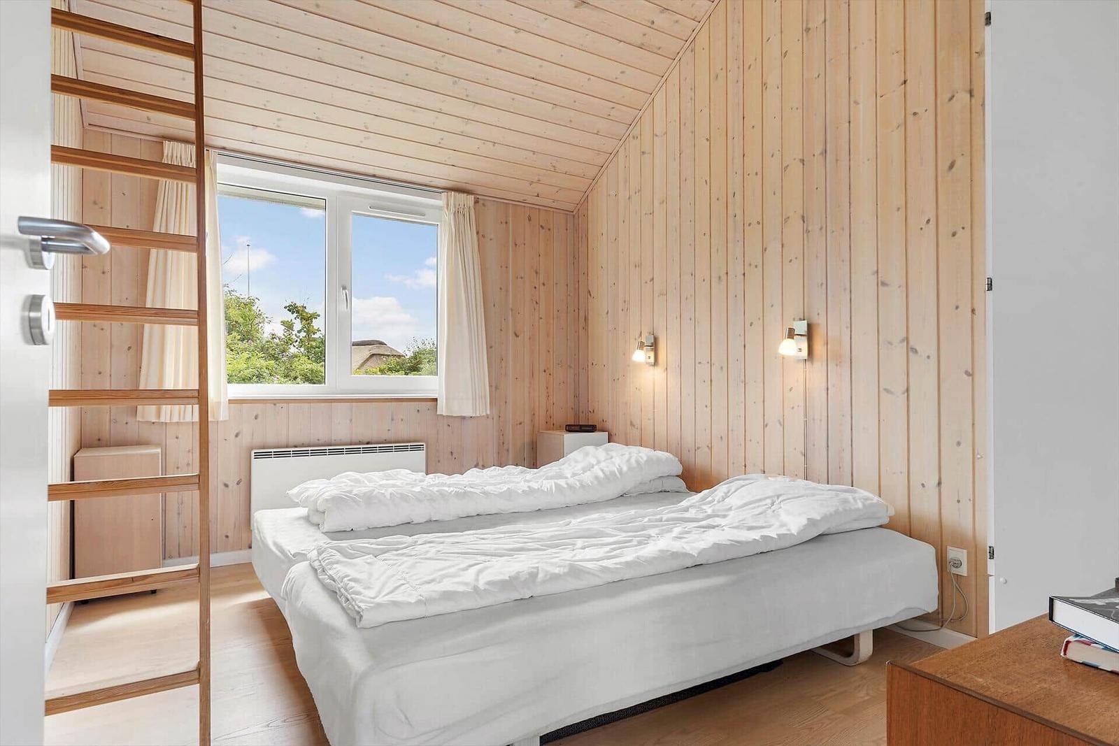 Schlafzimmer mit Holzwand, Fenster und Bett. Blick auf Gras und Himmel.