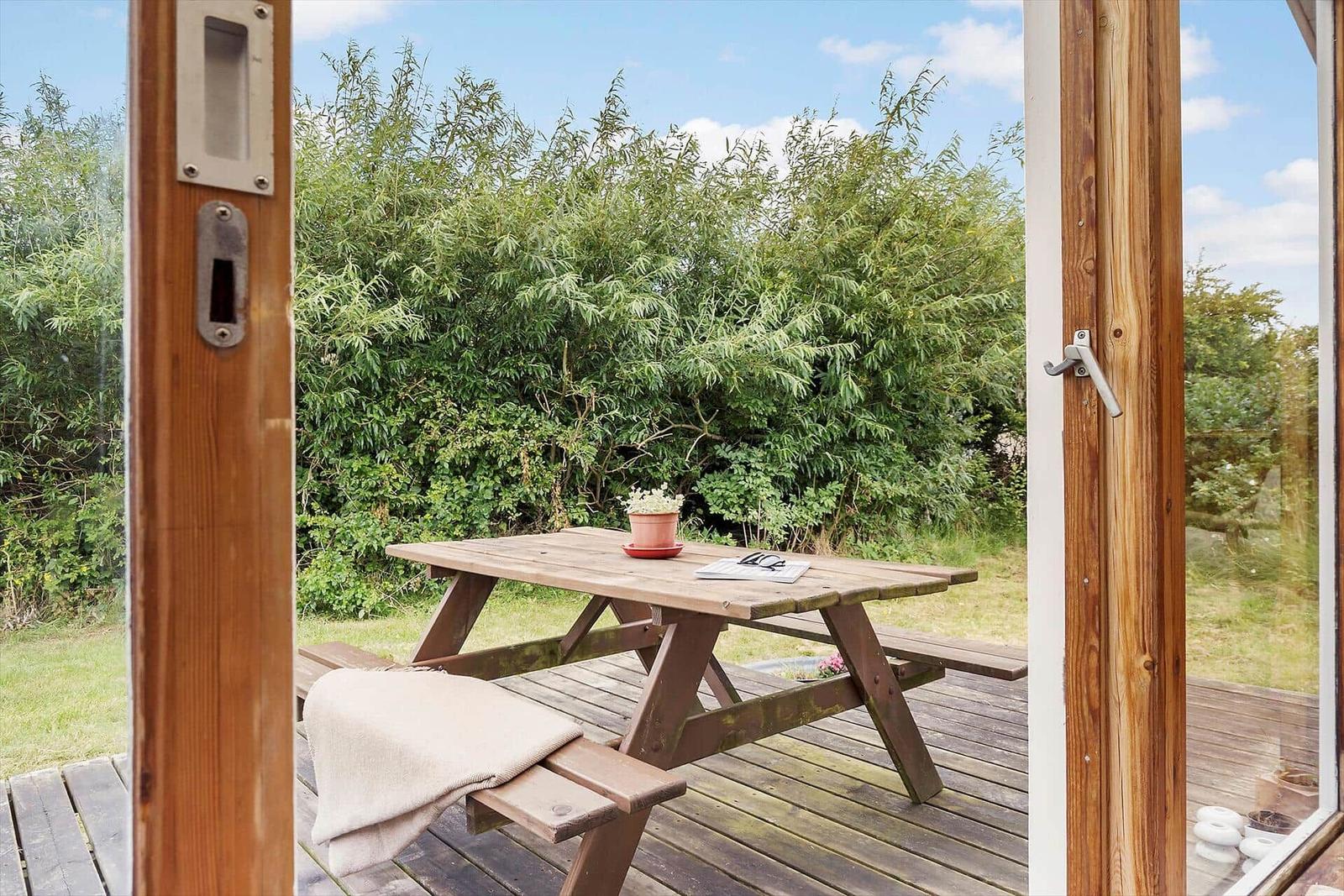 Haus mit Terrasse, Garten und Blick auf Hügel. Wein und Brille auf Tisch.