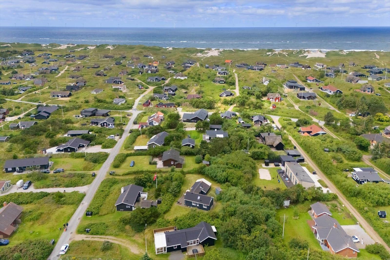 Haus mit orangefarbenem Dach auf Dünen, Blick auf das Meer und Windkraftanlagen.