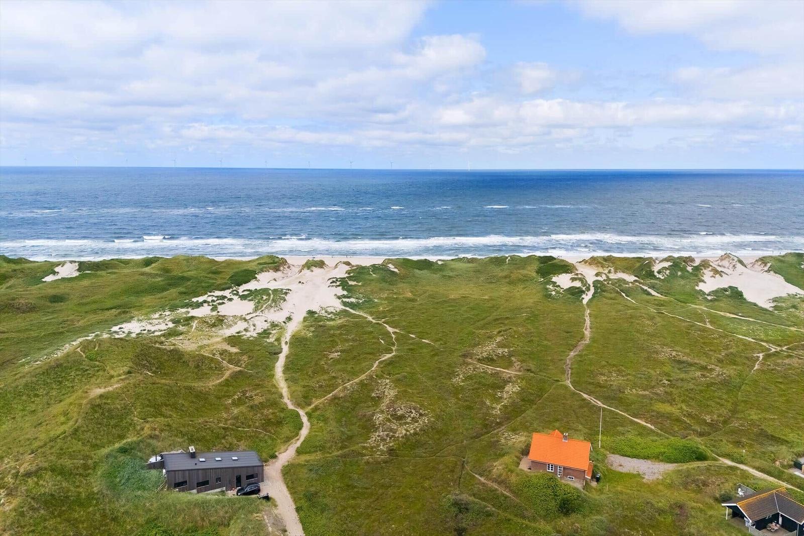 Strand mit Dünen und Häusern, Blick auf Wasser und Felder.