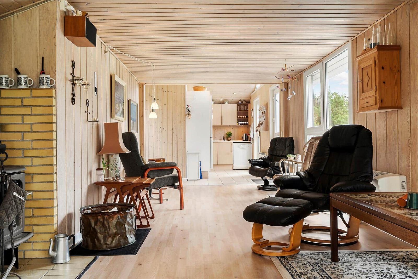 Wohnzimmer mit Holzdecke, Sofa, Couchtisch und Kamin. Durchgang zu Terrasse mit Garten.