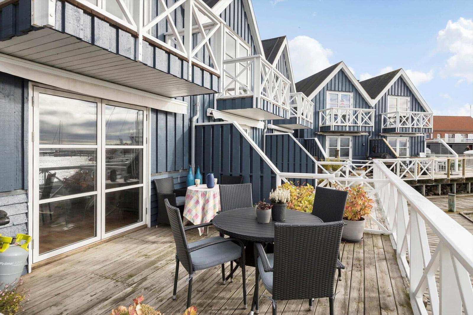 Terrasse mit Tisch und Stühlen, Blick auf Hafen mit Booten.
