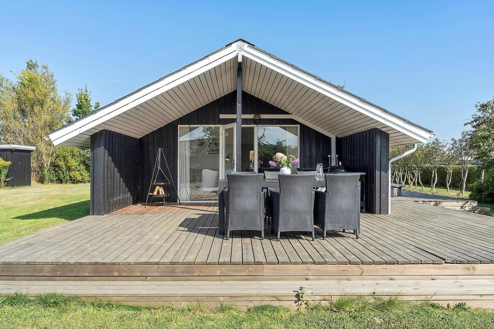 House with wooden terrace, sun lounger, and outdoor seating.