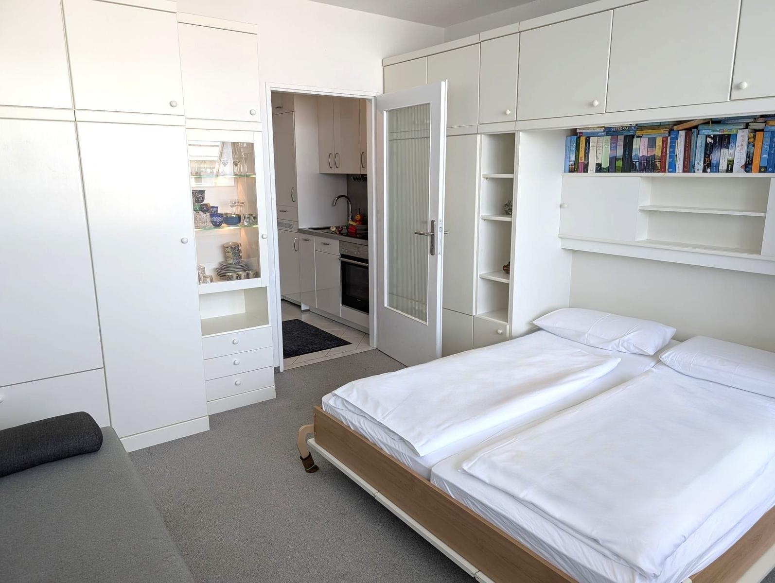 Schlafzimmer mit Doppelbett, weißer Schrankwand und Durchgang zur Küche.