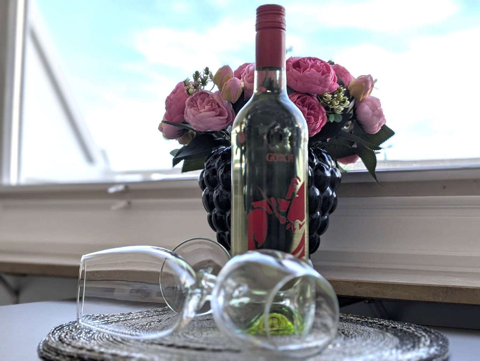 Liegende Weingläser, Weinflasche und rosa Blumen in dunkler Vase.