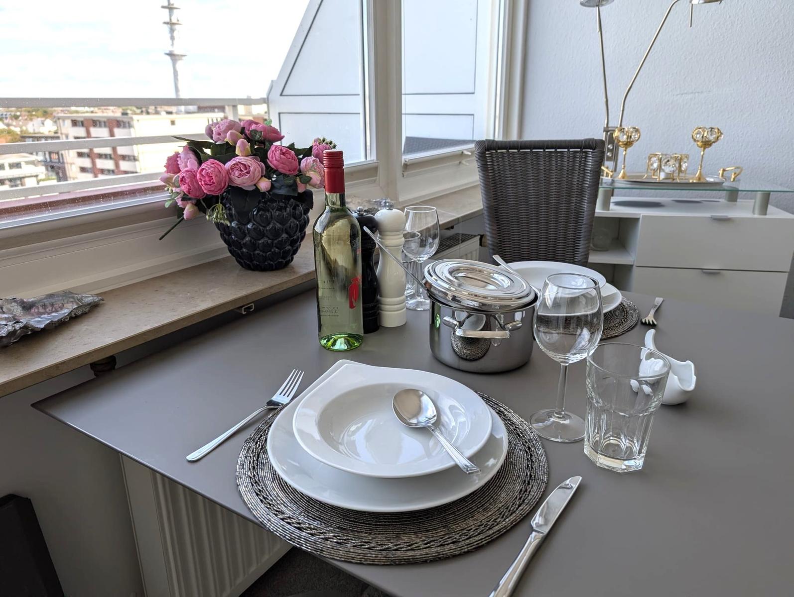 Esstisch mit Gedeck am Fenster, Weinflasche und Blick auf Stadt und Turm.