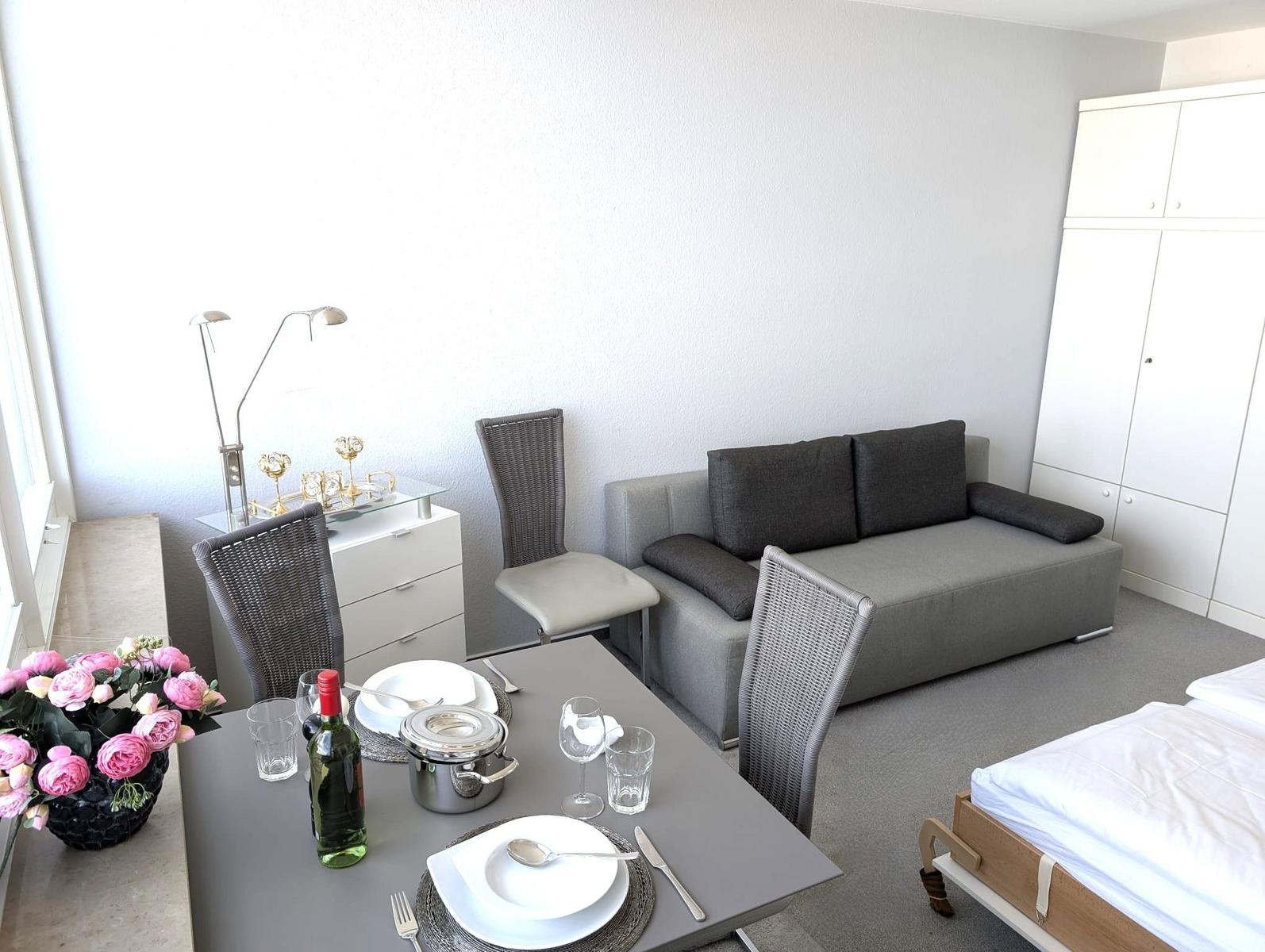 Esstisch mit Gedeck neben grauem Sofa und weißem Kleiderschrank.