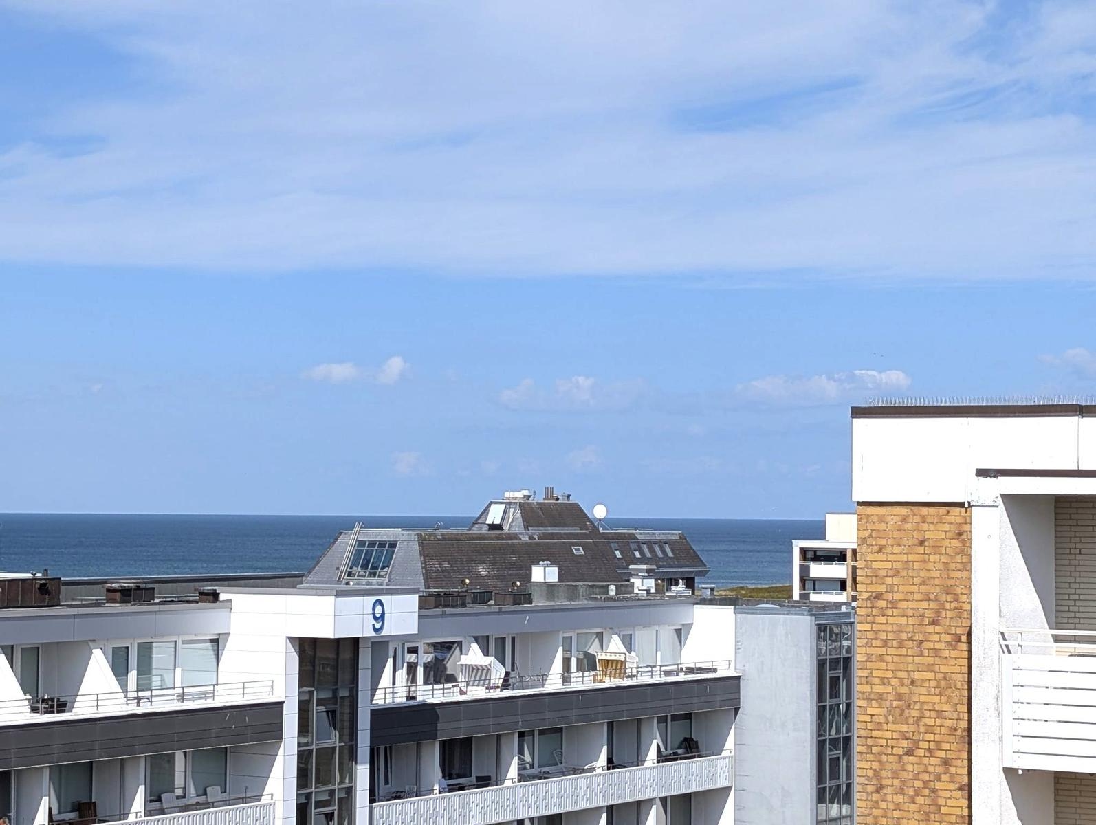 Blick über weiße Wohnbauten mit Balkonen und Strandkörben auf das Meer.
