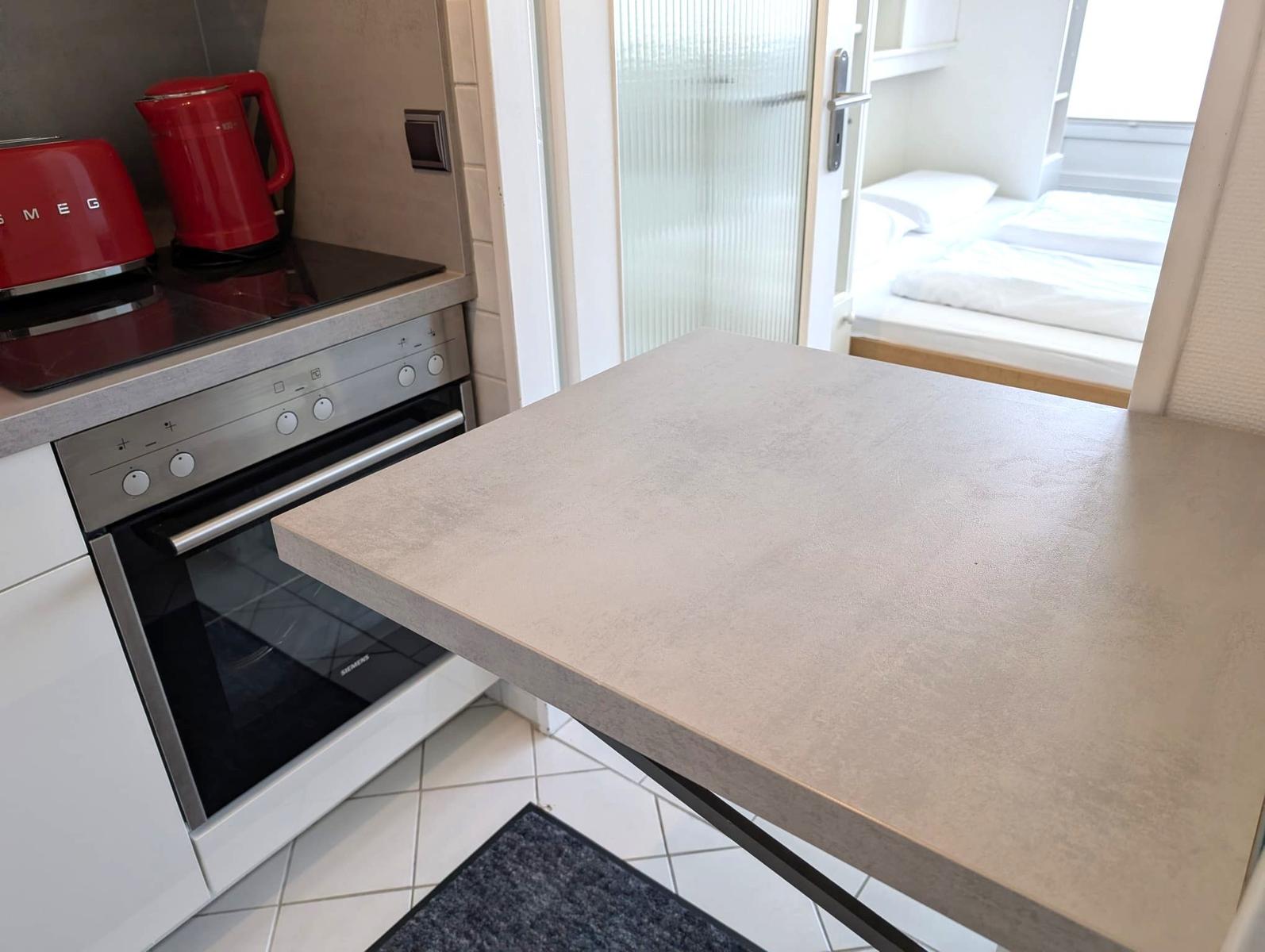 Küchenzeile mit Ceranfeld, rotem Toaster und Blick ins Schlafzimmer.