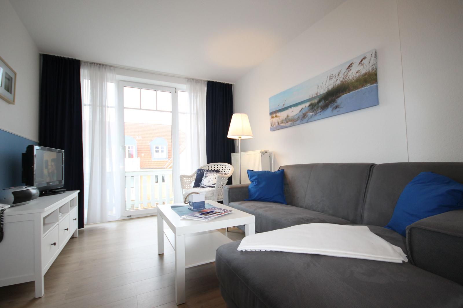 Wohnzimmer mit Sofa, Couchtisch und TV. Balkon mit Sicht auf Gebäude.