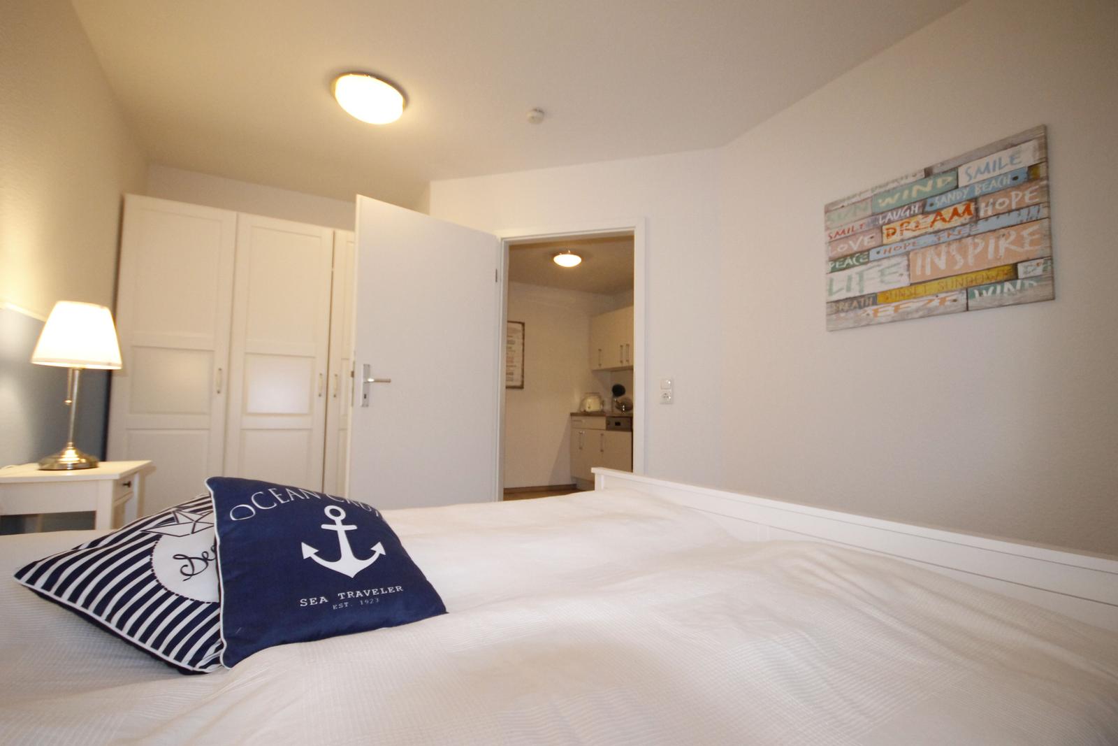 Schlafzimmer mit Bett, Kissen und Wandbild. Tür führt in die Küche.
