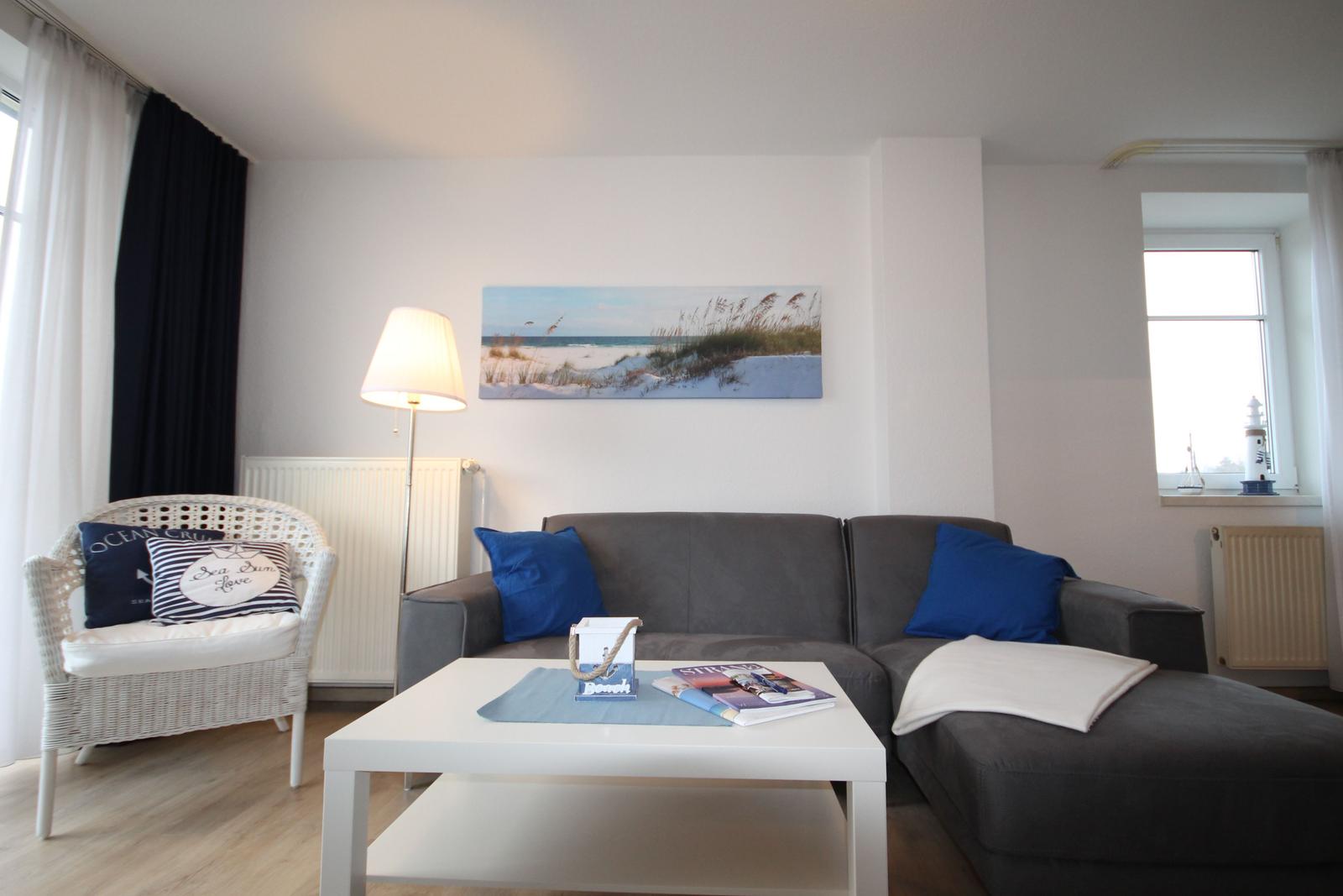 Wohnzimmer mit grauem Sofa, weißem Tisch und Strandbild an der Wand.