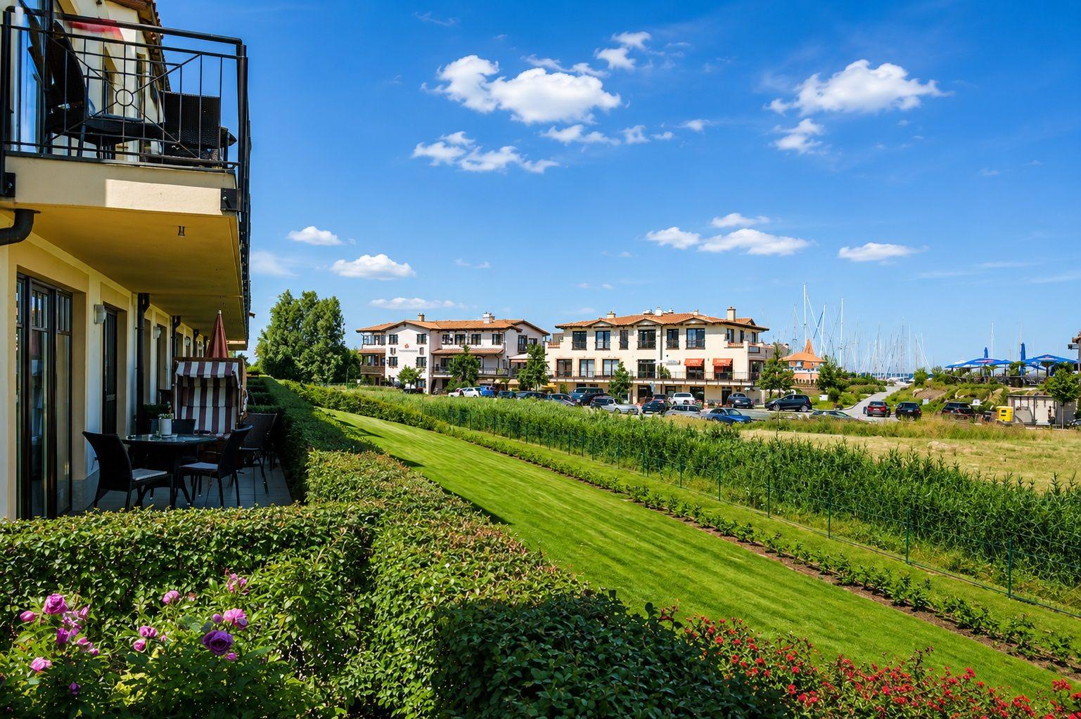 Terrasse mit Sitzgelegenheiten, Blick auf grünen Rasenhang und Ferienhäuser im Hintergrund.