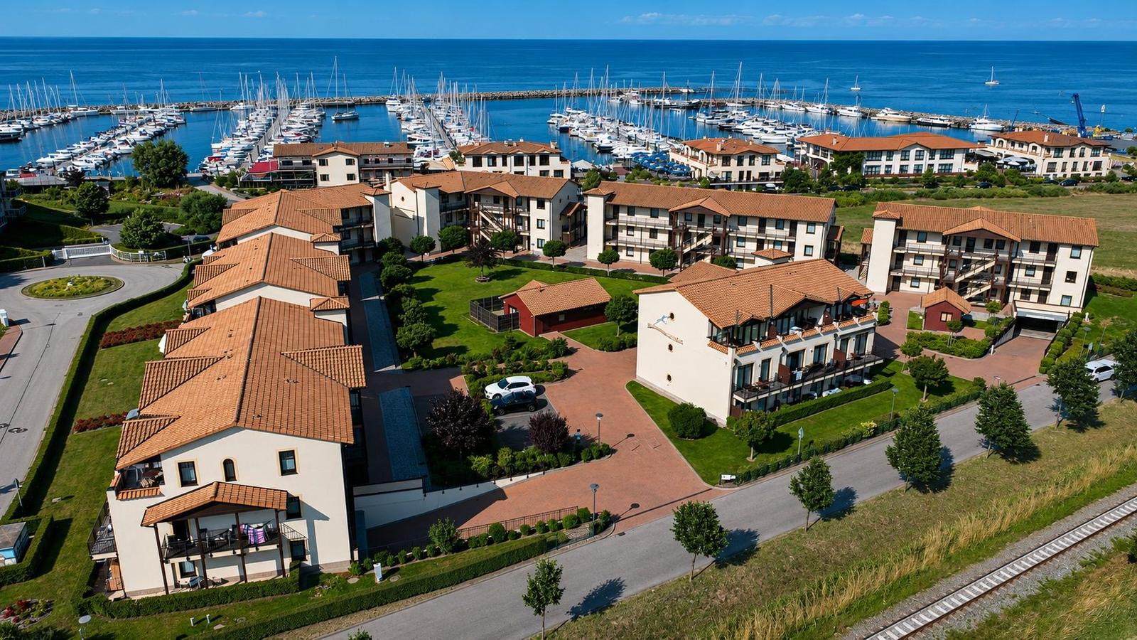 Wohnkomplex mit Terrassen und Blick auf Hafen mit Booten.