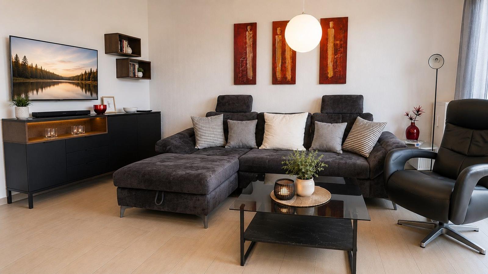 Ein Wohnzimmer mit grauem Sofa, Glas-Tisch und roten Wandbildern.