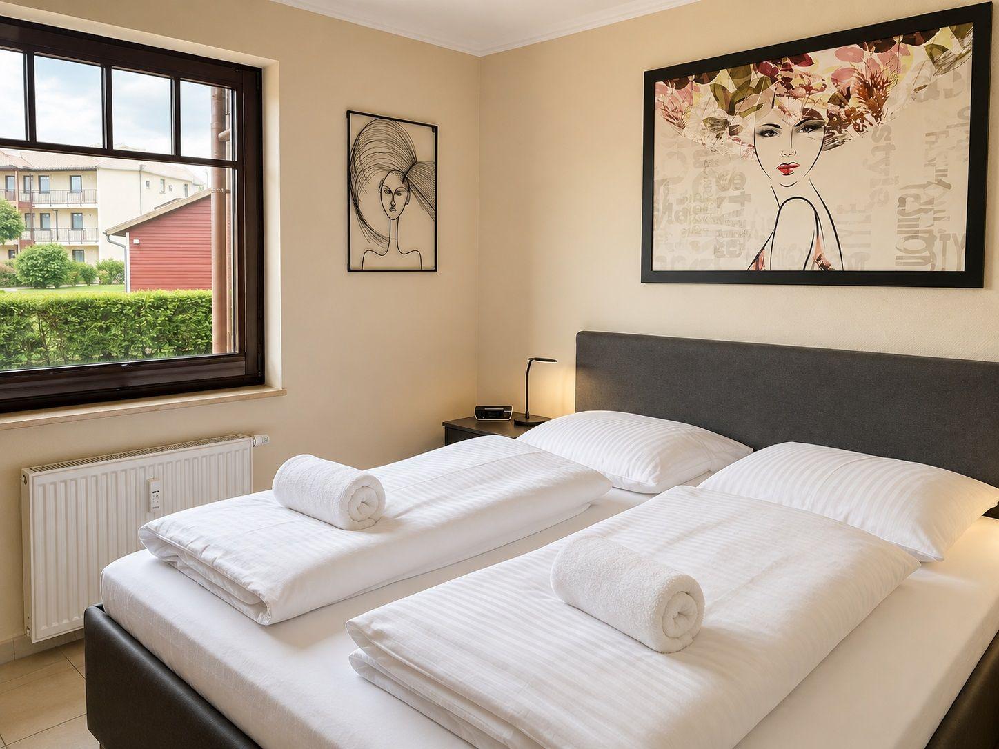 Schlafzimmer mit Doppelbett, Fenster und Wandbildern.