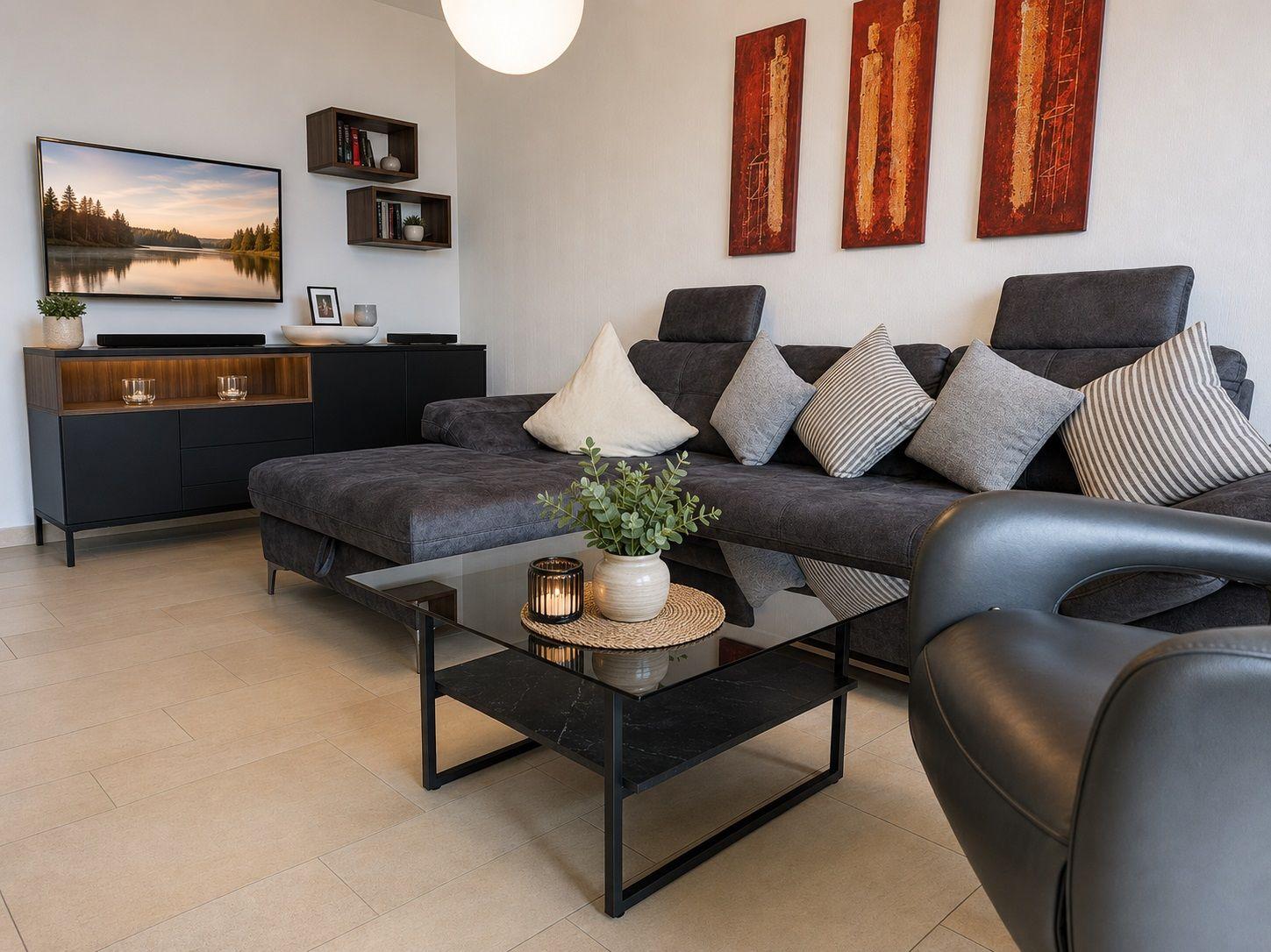 Ein Wohnzimmer mit grauem Sofa, Glas-Tisch und Wandbildern.