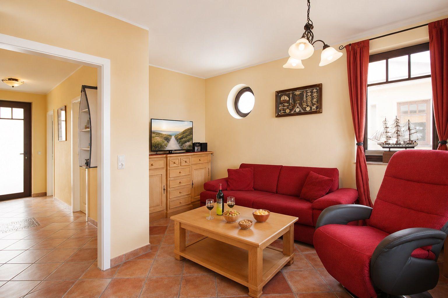 Wohnzimmer mit rotem Sofa, Holztisch und Fernseher. Fenster mit roten Vorhängen.