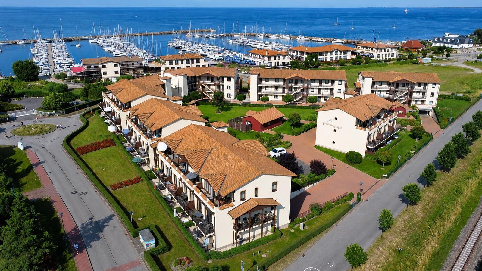Meerfrontanlage mit mehreren Gebäuden, Terrassen und Bootshafen im Hintergrund.