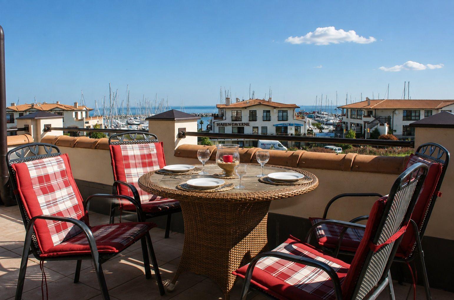 Terrasse mit Tisch und Stühlen, Blick auf Hafen und Meer.