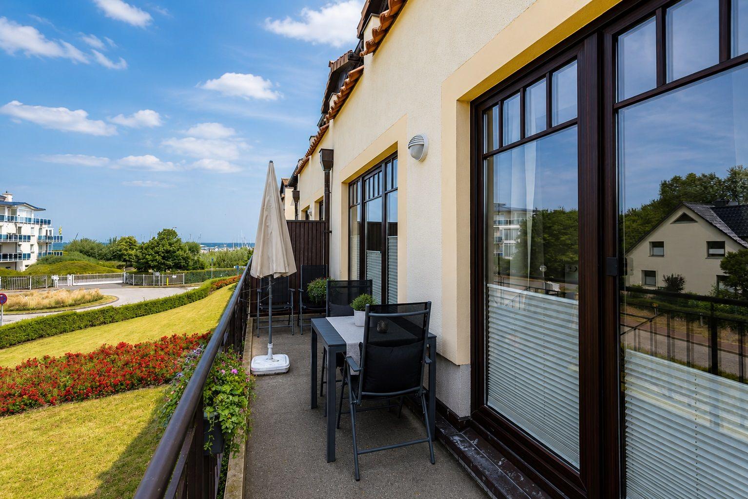 Terrasse mit Tisch, Stühlen und Sonnenschirm. Blick auf Grünflächen und Gebäude.