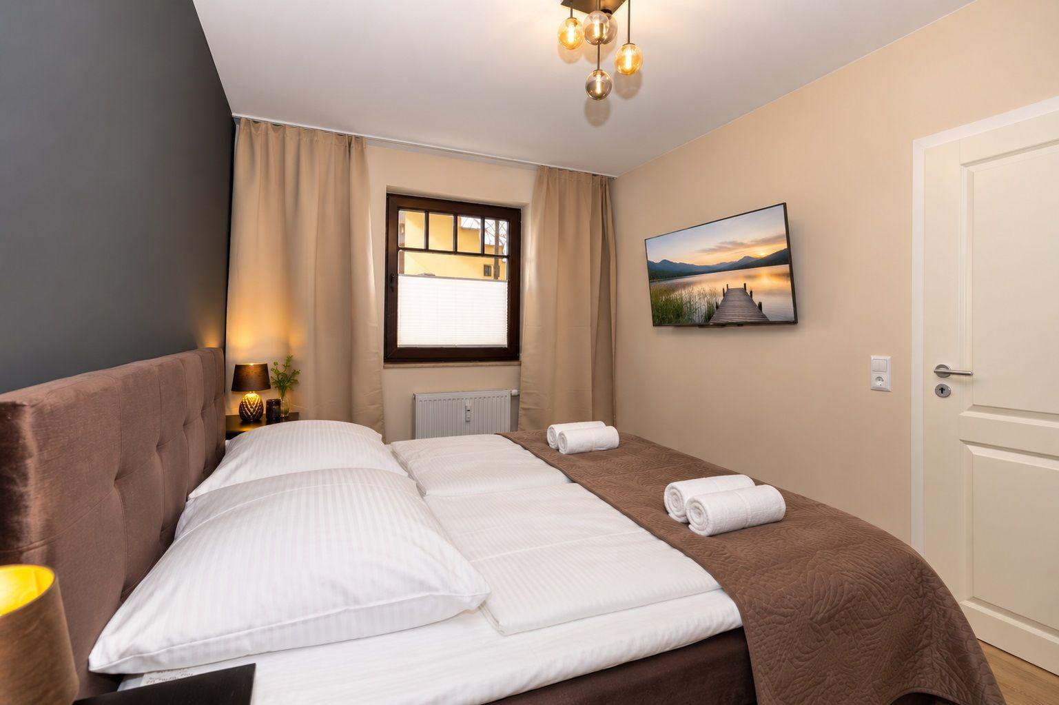 Schlafzimmer mit Bett, Fenster, TV und Lampe.