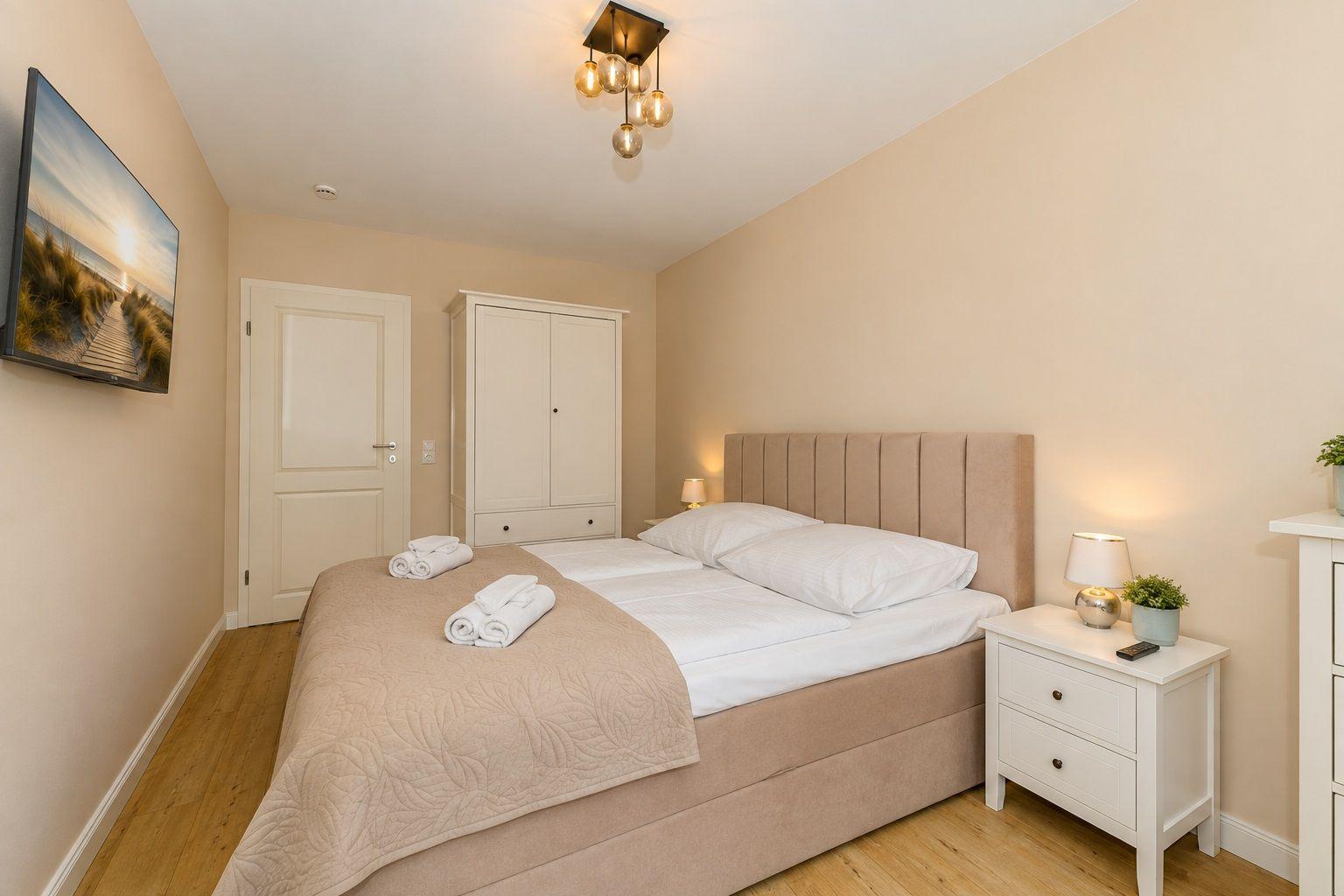 Schlafzimmer mit Bett, Nachttisch, Kleiderschrank und Wandfernseher.