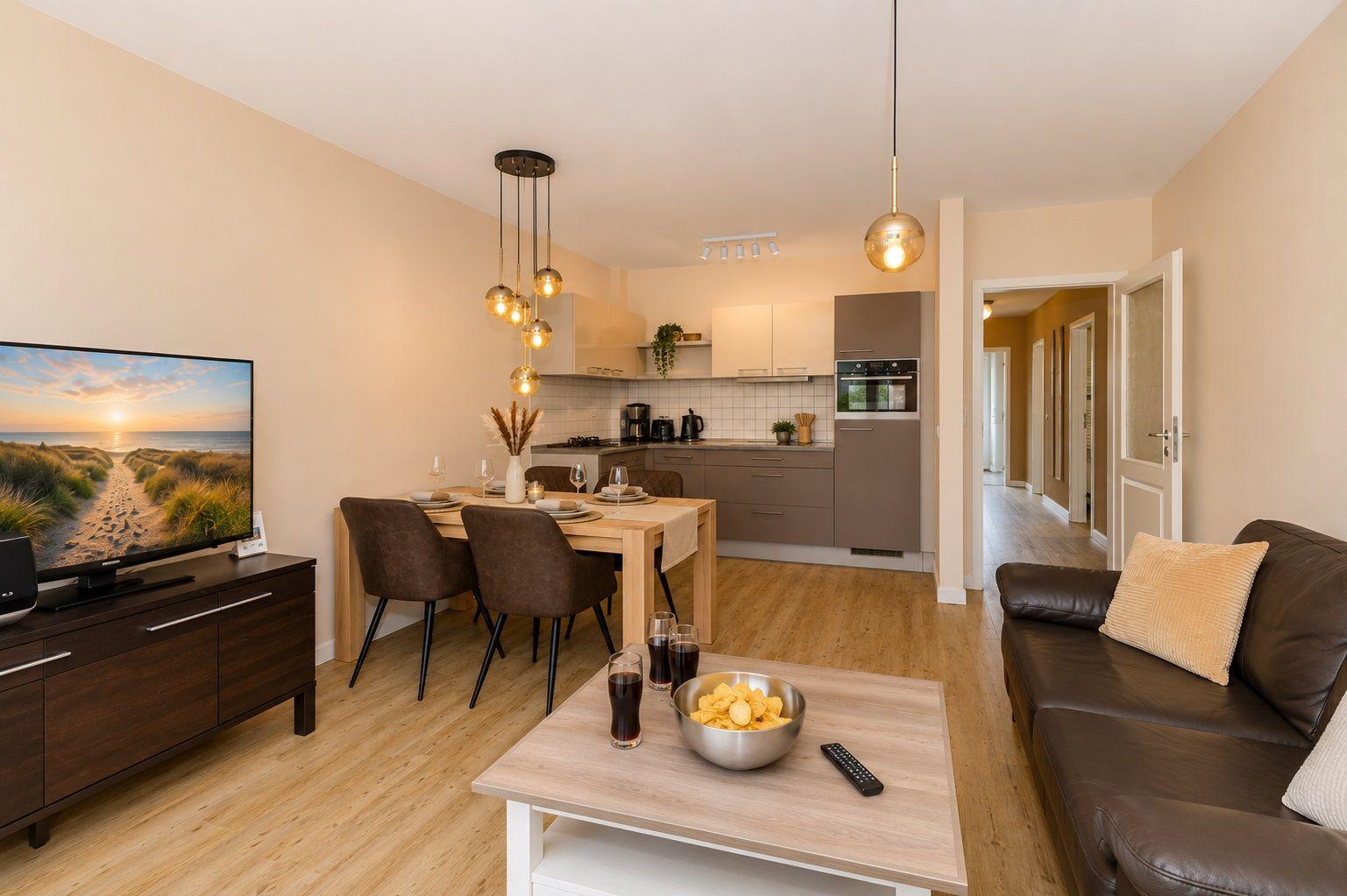 Wohn- und Essbereich mit Küche und TV. Holzboden und moderne Beleuchtung.