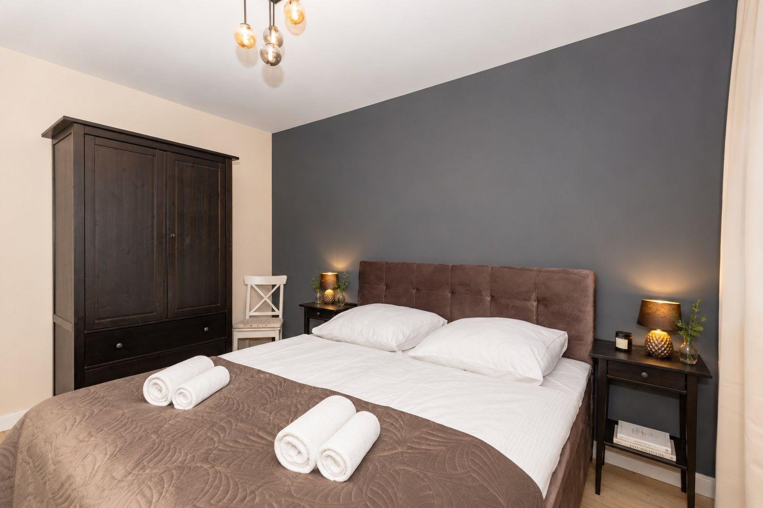Schlafzimmer mit Bett, Nachttischen und Kleiderschrank an grauer Wand.