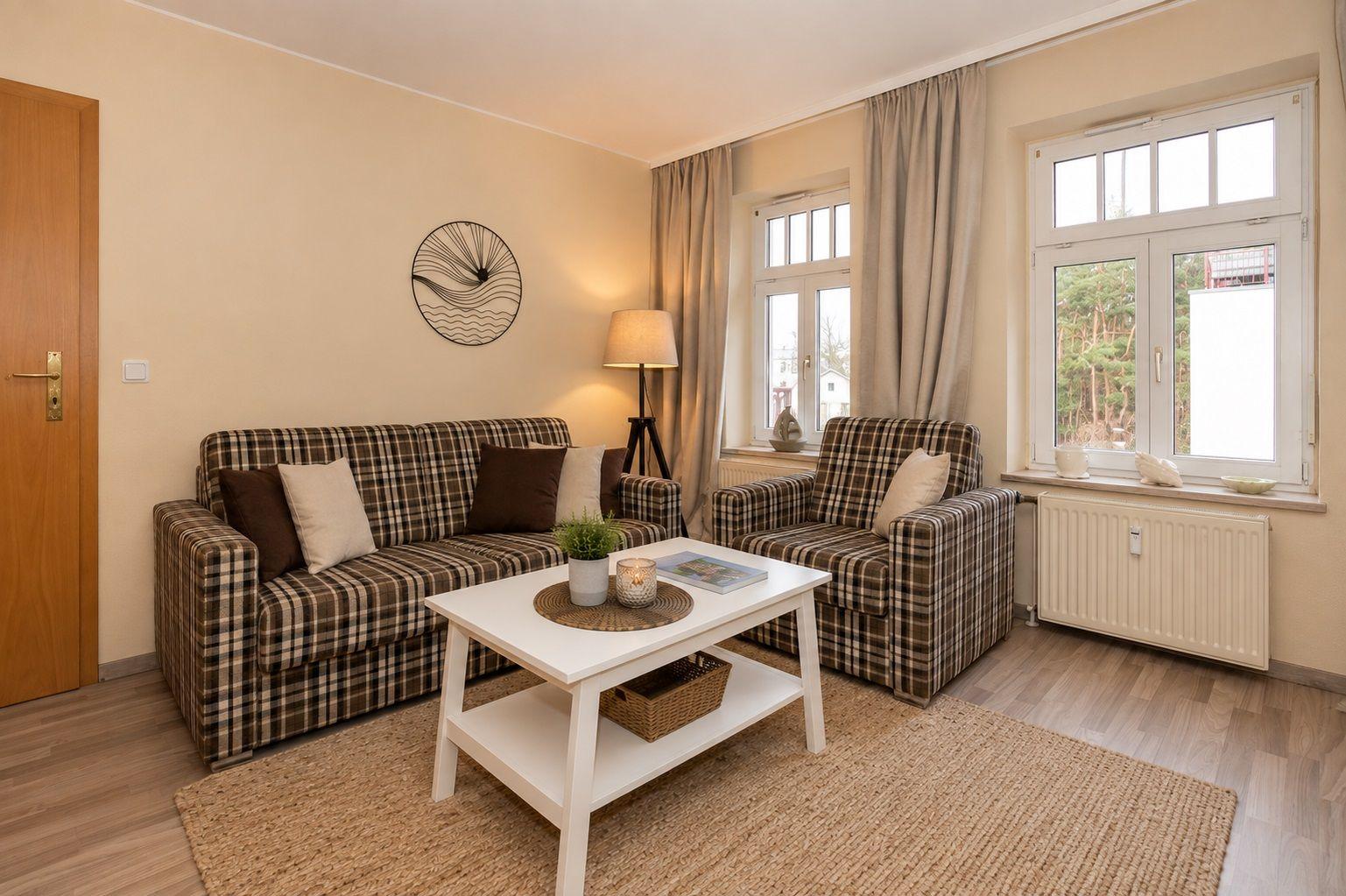Living room with sofa, armchair, and table. Windows with view of forest.