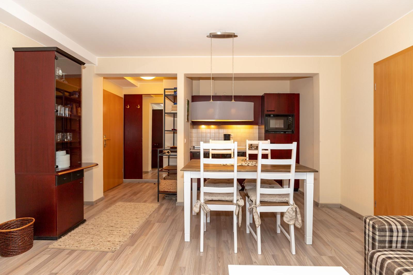 Dining area with table and chairs, kitchen with range hood and microwave, wooden floor and living area.