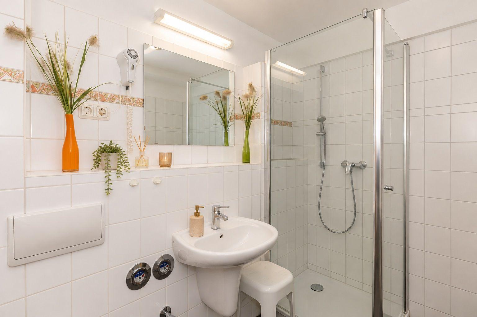 Bathroom with shower, sink, and mirror. Orange and green vases decorate the room.