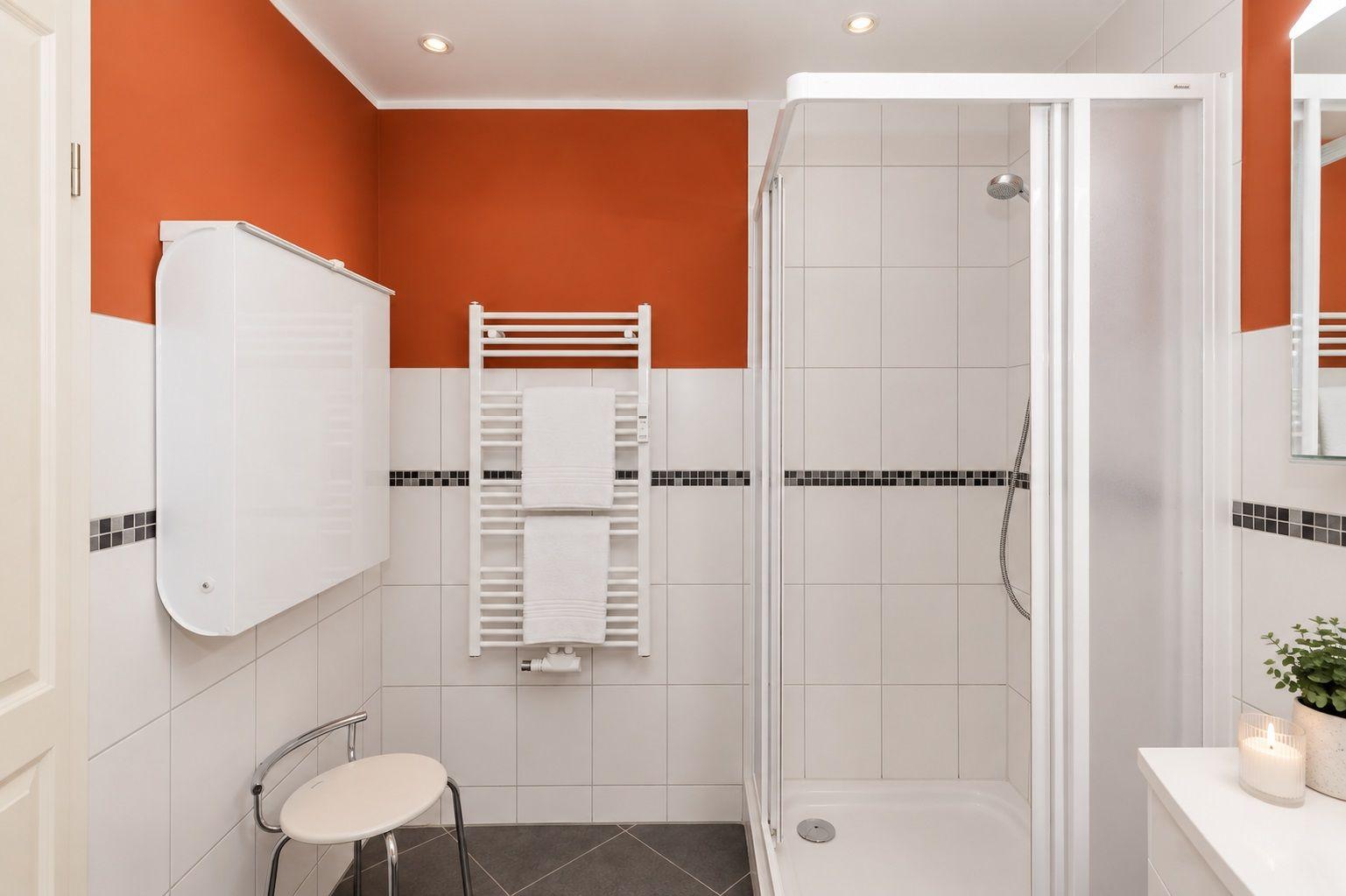 Badezimmer mit orangefarbenen Wänden, weißer Fliesenwand und Waschbecken.