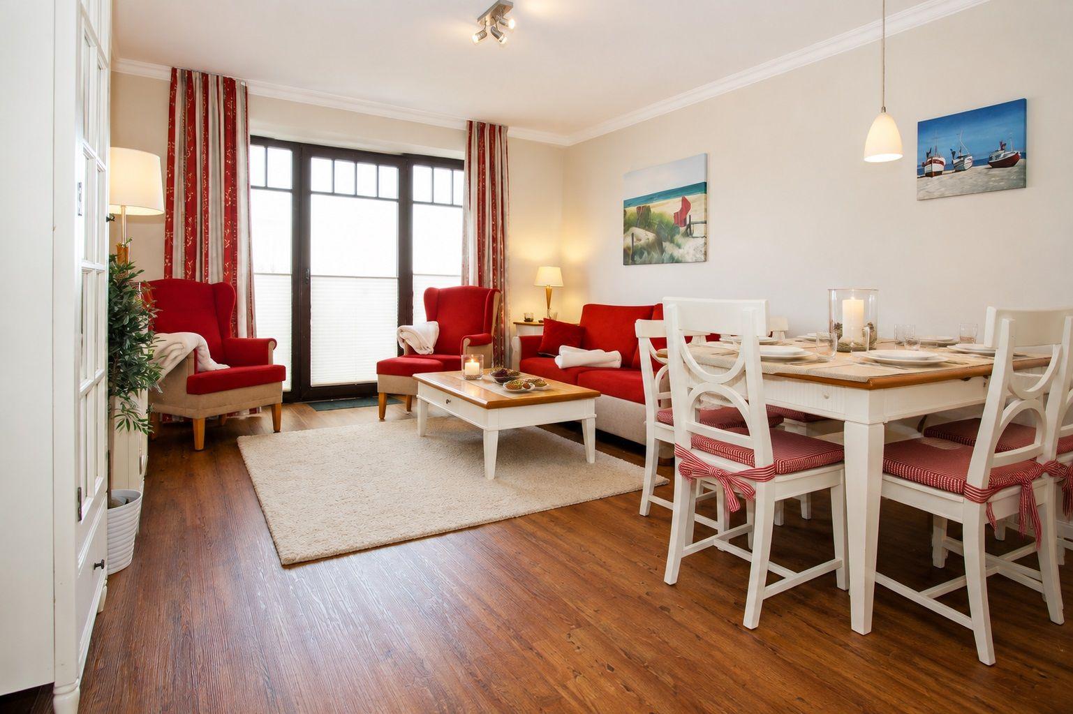 Wohn- und Essbereich mit rotem Sofa, weißen Stühlen und Holzboden.