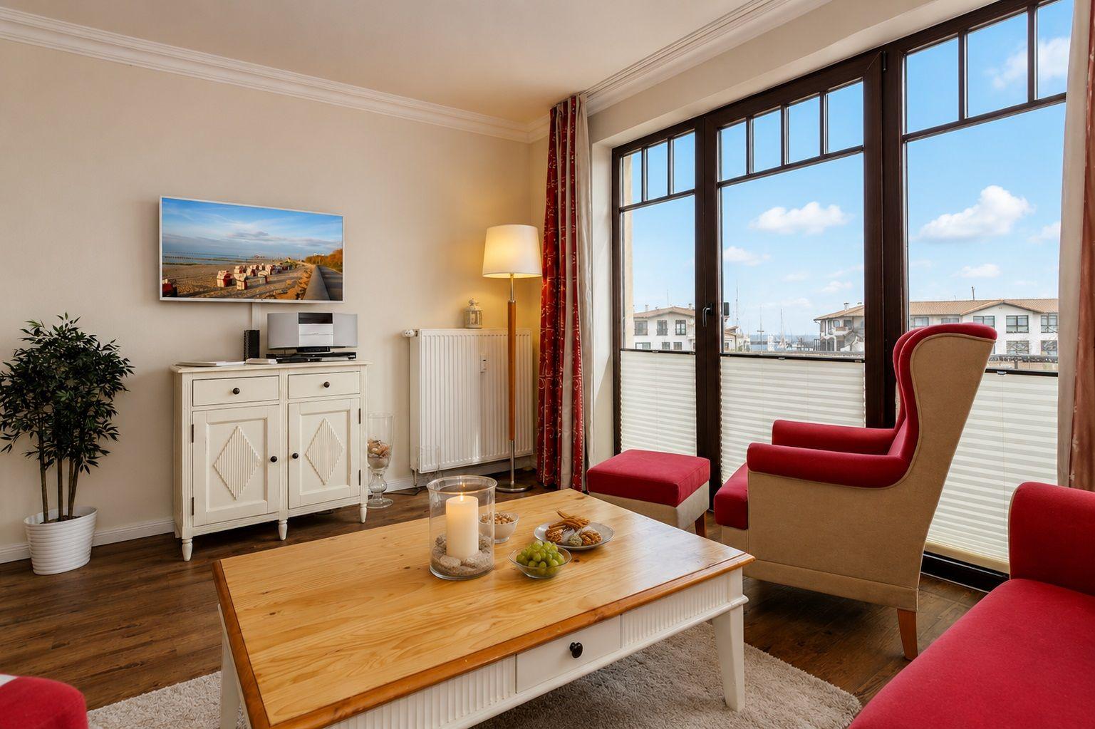 Wohnzimmer mit rotem Sessel, Holztisch und TV an der Wand.