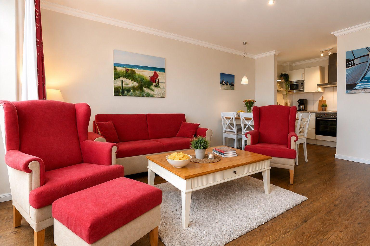 Wohnzimmer mit roten Sesseln, Sofa und Holztisch. Küche im Hintergrund.