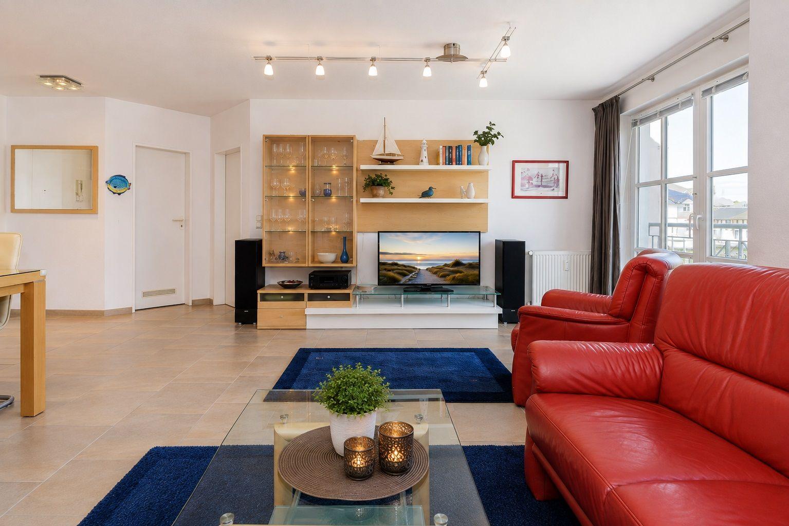 Ein Wohnzimmer mit rotem Sofa, Glas-Tisch und Fernseher.