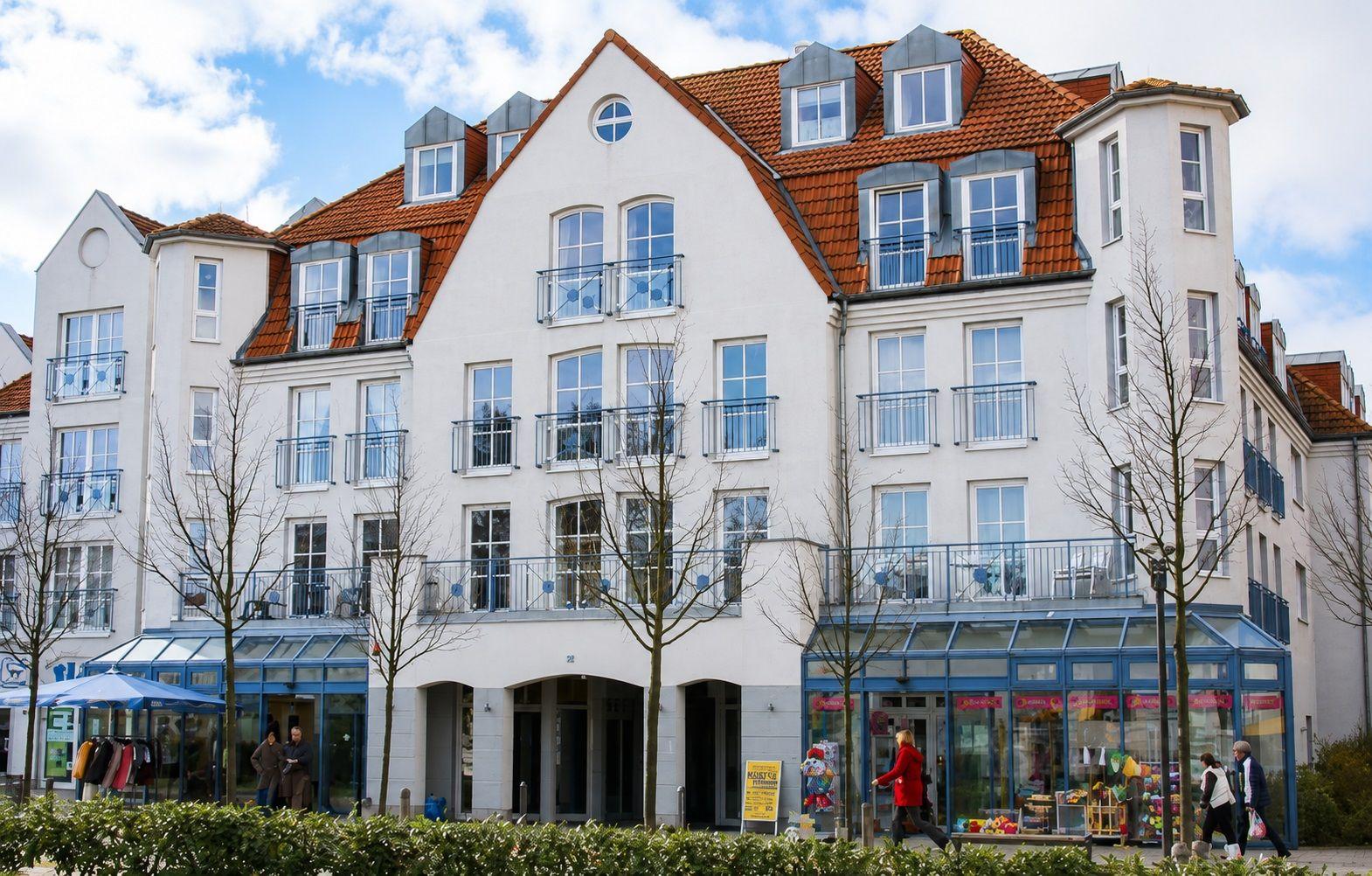Haus mit rotem Dach und weißen Wänden, Balkone und Geschäfte im Erdgeschoss.