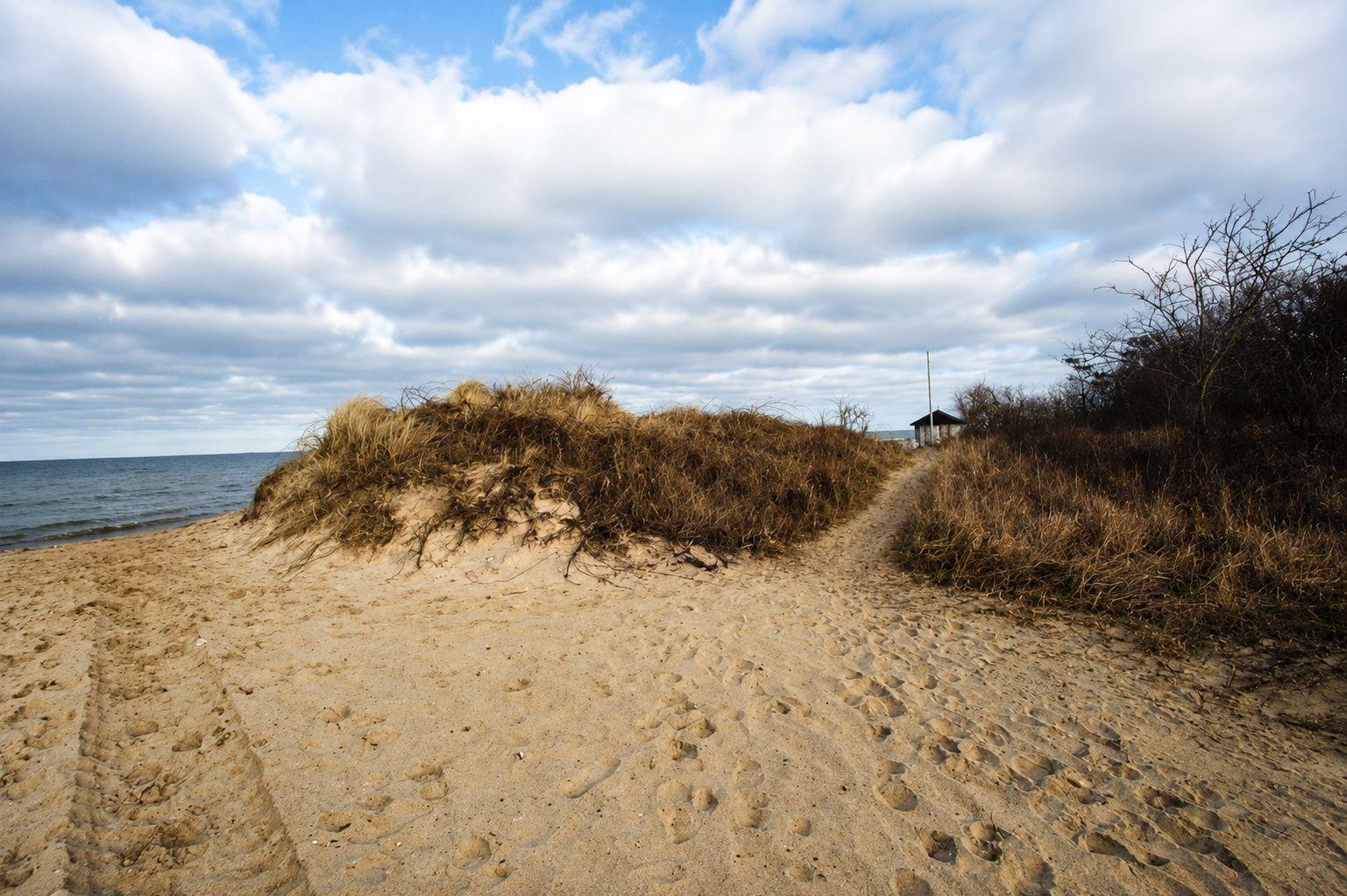 Weg durch Sanddünen zur Küste mit Blick aufs Meer unter bewölktem Himmel