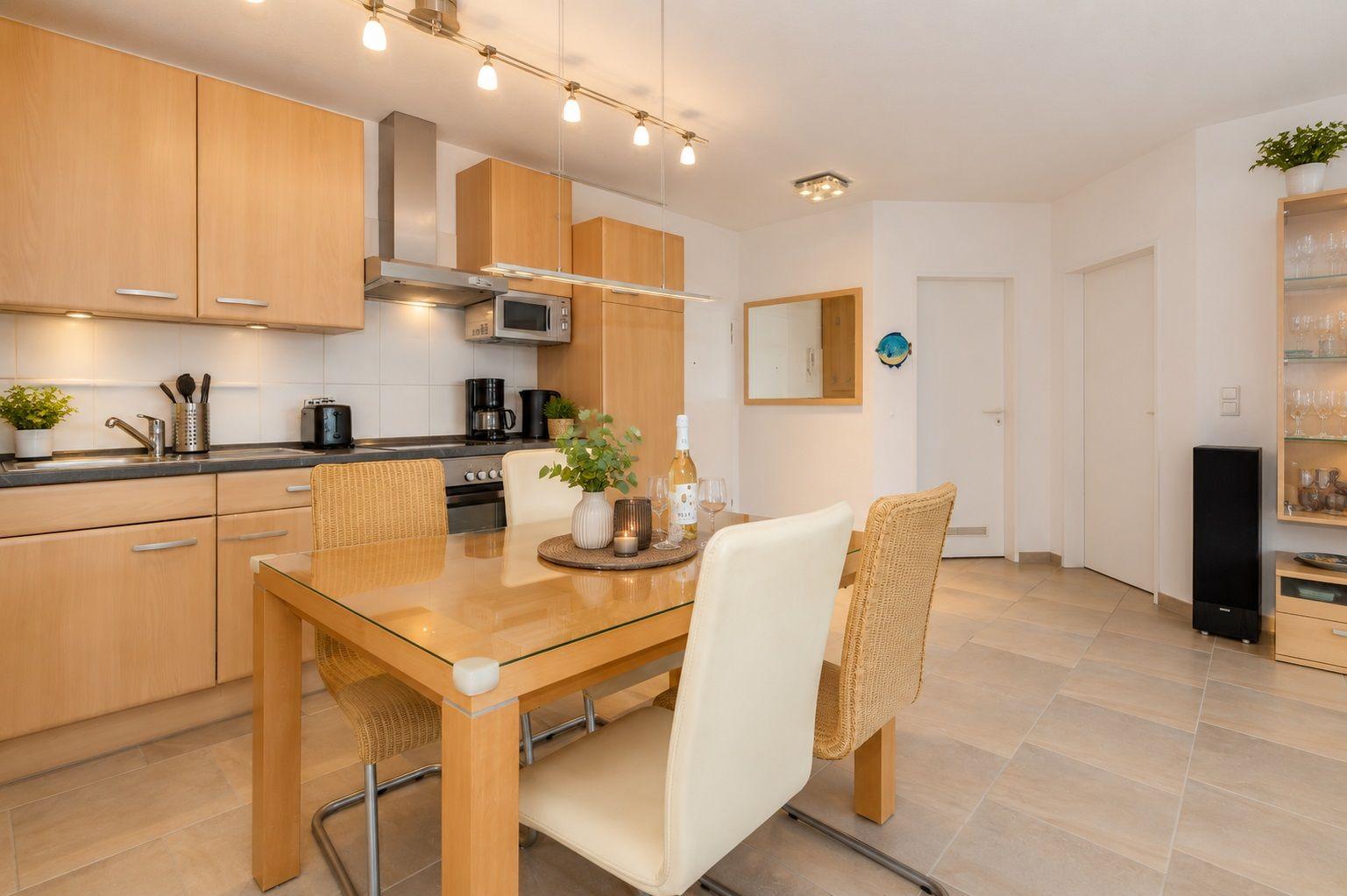Küche mit Essbereich, Holzmöbel und Glasplatte. Hintergrund: Flur mit Tür und Spiegel.