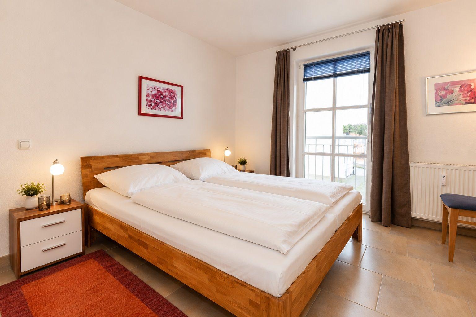 Schlafzimmer mit Doppelbett, Nachttisch und Fenster zum Balkon.