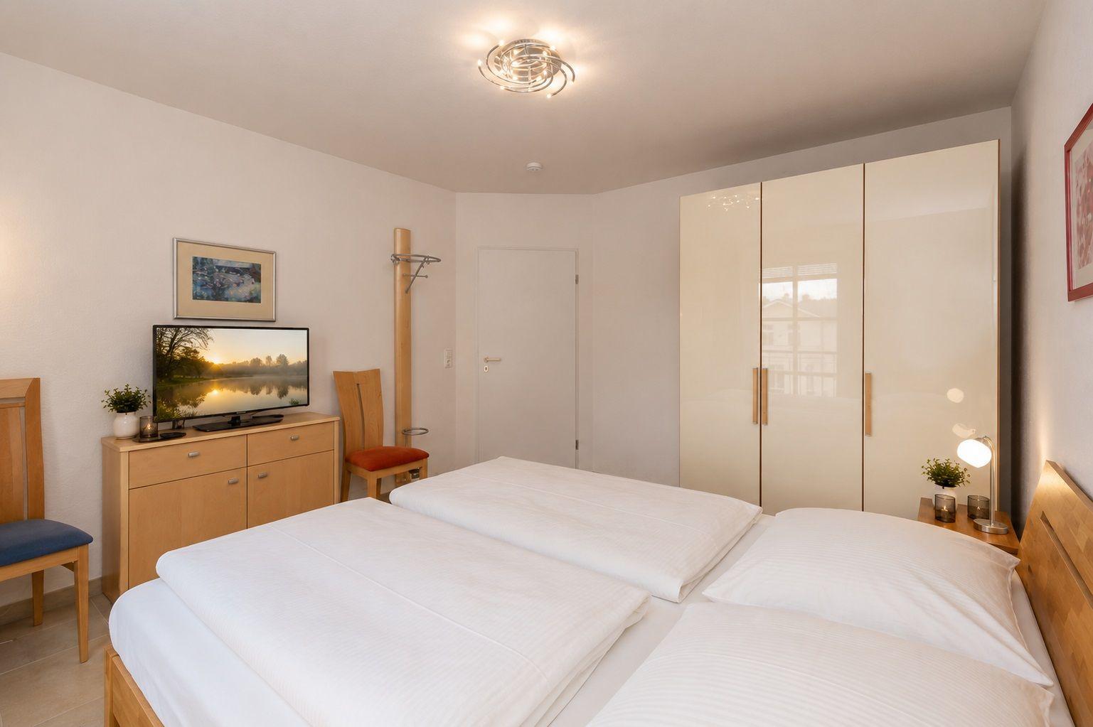 Schlafzimmer mit Doppelbett, Kleiderschrank und Fernseher auf Holzschrank.